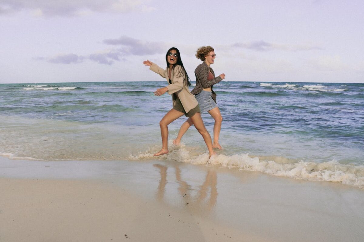 Two friends enjoying a run along the sunny beach, capturing carefree summer vibes.